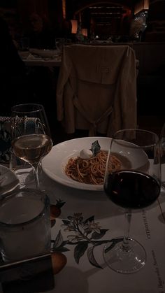 a plate of spaghetti and two glasses of wine on a table in a dimly lit room