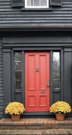 two flower pots with yellow mums sit in front of a red door on a black house