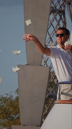 a man in white shirt and sunglasses throwing money into the air on top of a boat