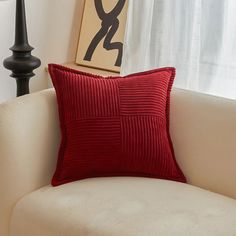 a red pillow sitting on top of a white couch next to a lamp and window