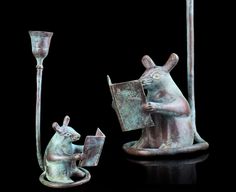 a statue of a mouse reading a book next to a candle holder with a lamp on it