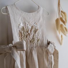 a dress hanging up on a wall next to dried flowers and grass blades with the back tie down