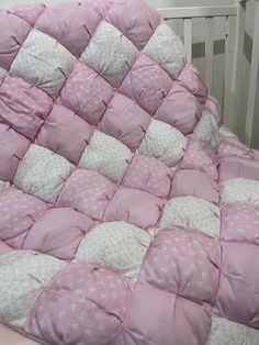 a baby crib with pink and white quilted bedding on top of it