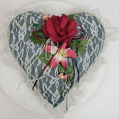 there is a heart shaped box with flowers in it on the table next to a lace doily