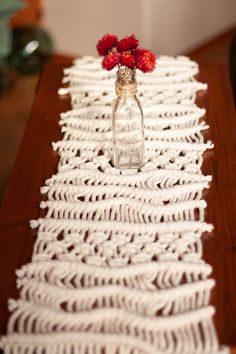 a vase with red flowers sitting on top of a wooden table next to a white crocheted runner