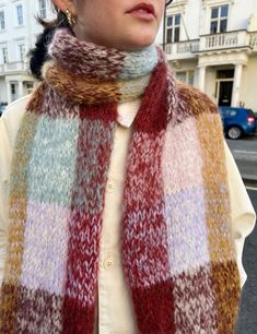 a woman wearing a multicolored scarf standing in front of a building on the street