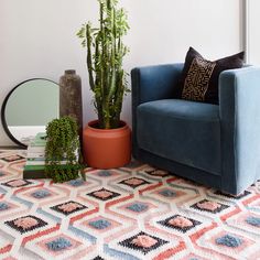 a living room with a blue chair, potted plant and mirror on the floor