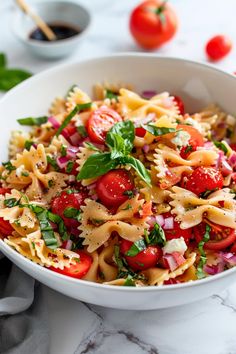 a white bowl filled with pasta salad and topped with tomatoes, onions, spinach