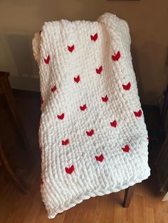 a white crocheted blanket with red hearts on it sitting on top of a wooden chair