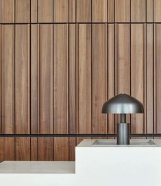 a lamp sitting on top of a white table next to a wall covered in wooden slats