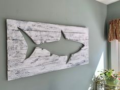 a wooden shark cut out on the wall next to a potted plant and window