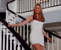 a woman in a white dress is walking down the stairs with her hand on her hips