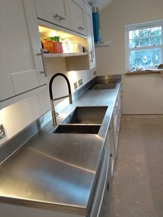 a stainless steel kitchen sink in the middle of a room with white cabinets and drawers