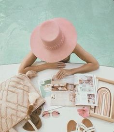 a woman sitting at a table next to a pool with her hat on top of it