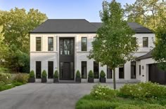 a large white house with black doors and windows in the front yard is surrounded by greenery