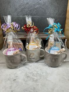 three coffee mugs wrapped in cellophane and decorated with bows are sitting next to each other