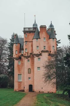 an old pink castle with two towers on the top and one at the bottom, surrounded by trees