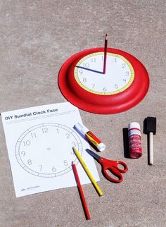 a red clock with markers, scissors and glue on the ground next to it is an activity for kids