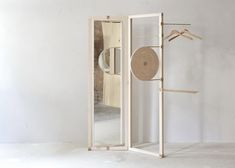 an open door with clothes on hangers and a mirror in the middle, against a white wall