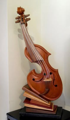 a violin sculpture sitting on top of a pile of books next to a white wall