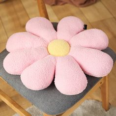 a pink flower shaped cushion sitting on top of a chair with a wooden leg rest