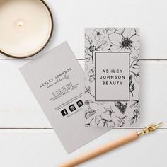 a white and black floral business card next to a candle on top of a table