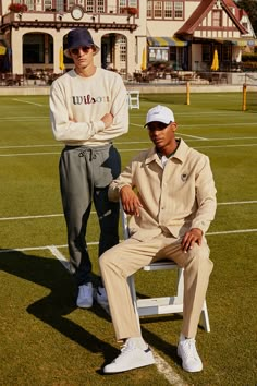 two men sitting on a bench in front of a building with a field behind them