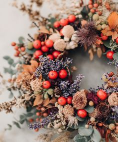 a wreath with red berries, oranges and other flowers on it's side