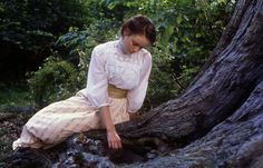 a woman sitting on the ground next to a tree