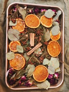 an arrangement of dried oranges, cinnamon sticks and herbs in a metal tray on a table