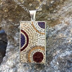 a necklace with a mosaic design on it sitting on top of a stone wall next to a rock