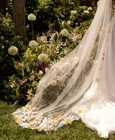 a wedding dress and veil sitting on the grass in front of some wildflowers