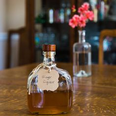 a bottle of liquor sitting on top of a wooden table next to a vase with flowers