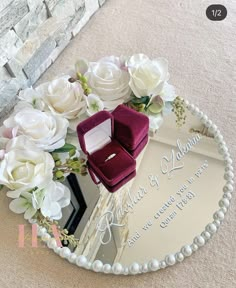 a wedding ring sits on top of a mirror with flowers and pearls around the edges