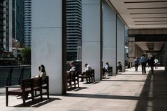 several people are sitting on benches in the middle of an empty walkway with tall buildings behind them