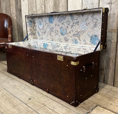 an old trunk sitting on top of a wooden floor next to a brown leather chair