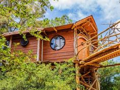 a tree house built on stilts in the woods with round windows and wooden railings