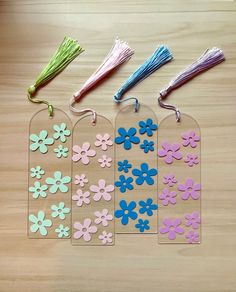 four tags with flowers and tassels attached to them on a wooden table top