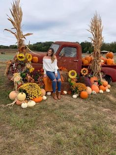 a woman sitting on the back of an old truck surrounded by pumpkins and sunflowers