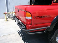 a red pick up truck parked in front of a building with its door open and the back end of it's bumper