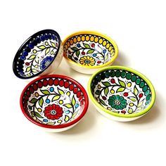 four colorful bowls sitting on top of a white table next to each other and one bowl has flowers painted on it