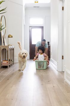 a man and his daughter are playing with their dog in the living room while they have laundry baskets on the floor