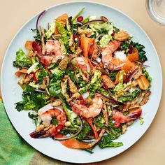 a salad with shrimp, lettuce and carrots on a plate next to a glass of water