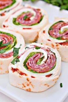 several rolls with meat, cheese and herbs on a white plate next to parsley