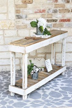 an old table with flowers on it in front of a brick wall and stone floor