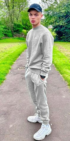 a young man is standing on the sidewalk wearing sweatpants and a baseball cap with his hands in his pockets