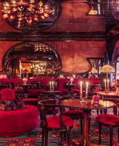 an ornately decorated restaurant with red velvet chairs and round tables in front of a large mirror