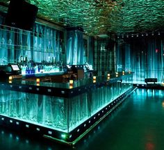 the bar is lit up with blue lights and green curtains on the ceiling above it