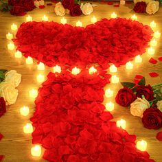 candles are lit in the shape of a heart and surrounded by roses on a wooden floor