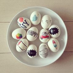 a white bowl filled with different types of painted eggs on top of a wooden table